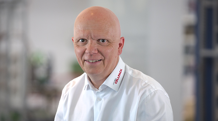 Smiling bald man in a white shirt, facing the camera in a bright indoor setting (portrait).
