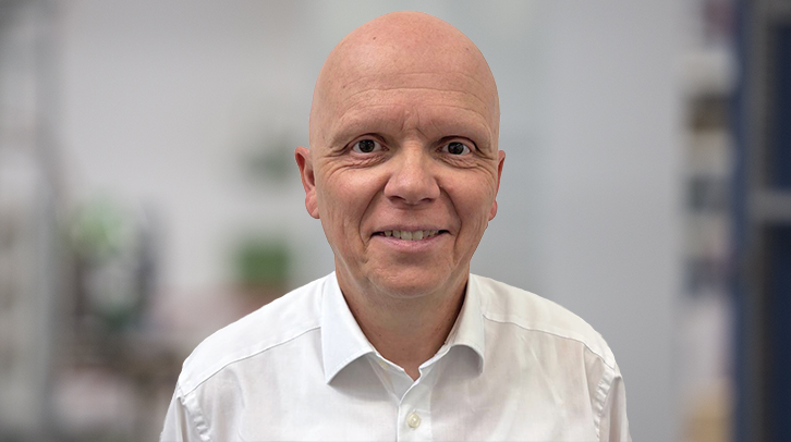 Smiling bald man in a white shirt, facing the camera in a bright indoor setting (portrait).